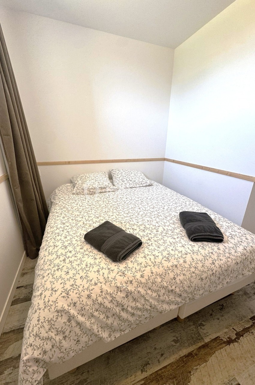 Lit double avec draps à motifs floraux, deux oreillers et deux serviettes pliées dans une chambre lumineuse.