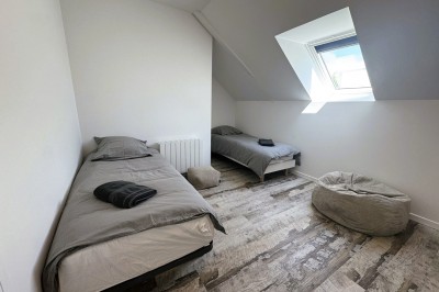 Chambre lumineuse avec lit double, parquet, portant à vêtements, chaise et fenêtre de toit.