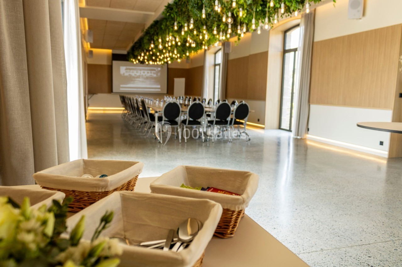 Salle de conférence lumineuse avec des chaises alignées, un écran de projection et un plafond décoré de plantes suspendues.