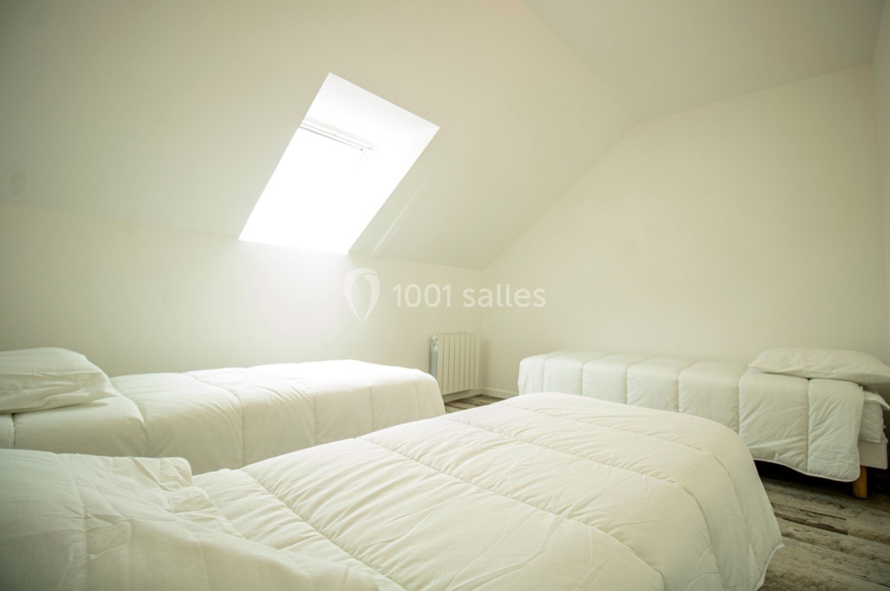 Chambre lumineuse sous les combles avec quatre lits simples alignés et un velux laissant entrer la lumière naturelle.