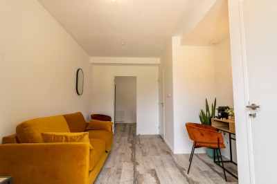 Chambre lumineuse avec lit double, parquet, portant à vêtements, chaise et fenêtre de toit.