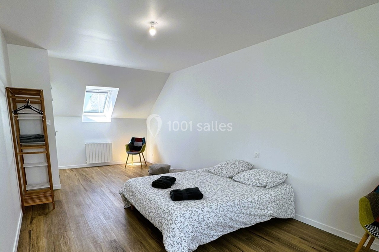 Chambre lumineuse avec lit double, parquet, portant à vêtements, chaise et fenêtre de toit.
