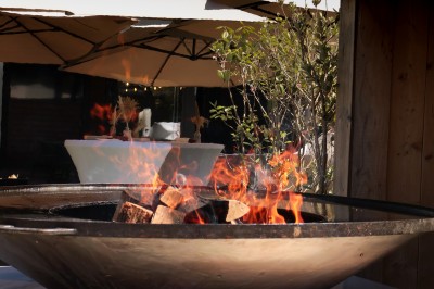 Miniature Location salle Toulouse (Haute-Garonne) - La Cantine d'Horace #18 Brasero allumé avec des flammes vives, placé sur une terrasse extérieure près d'arbustes et de parasols.
