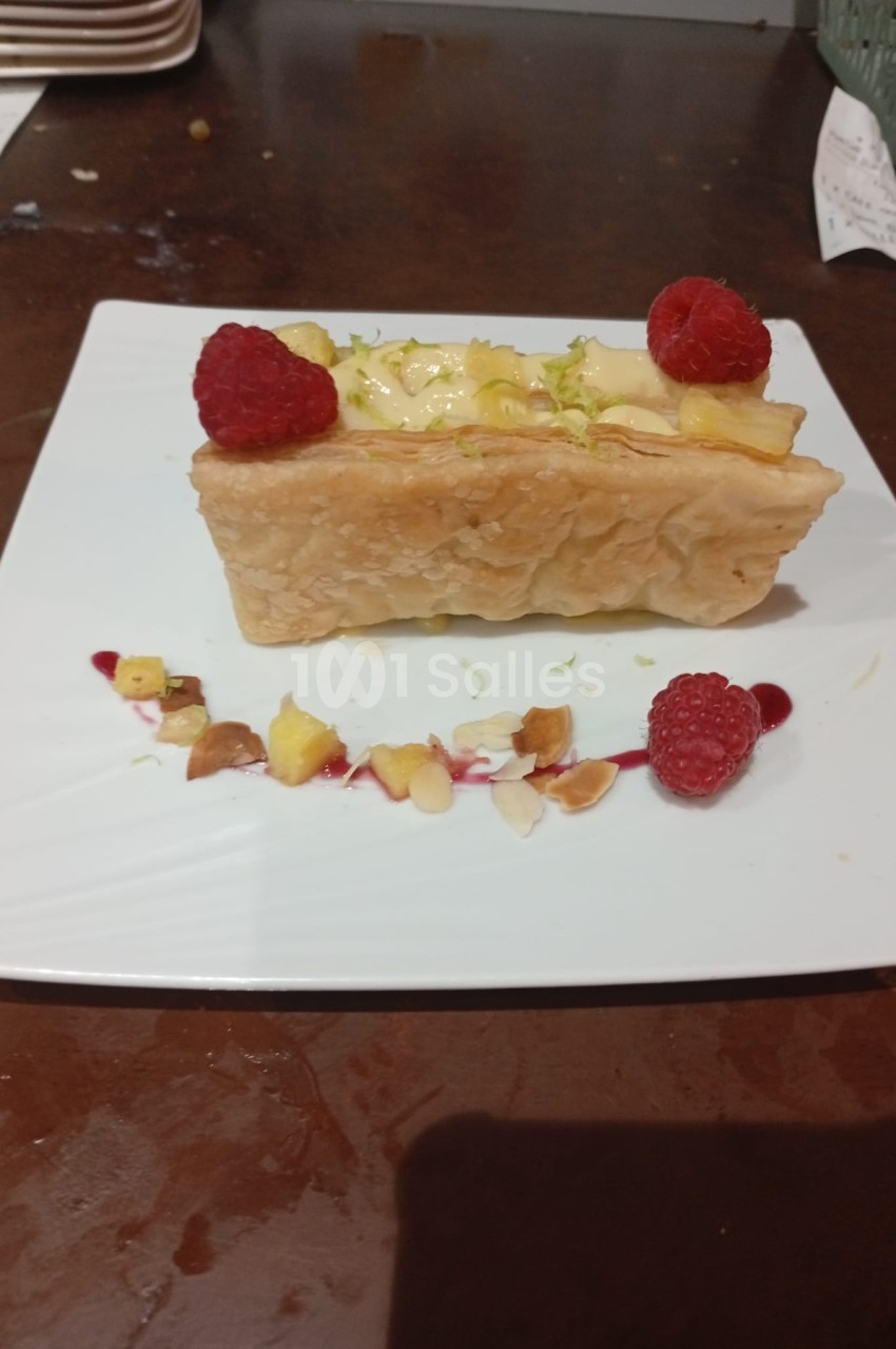 Dessert rectangulaire à base de pâte feuilletée, garni de crème et fruits, orné de framboises et pétales comestibles.