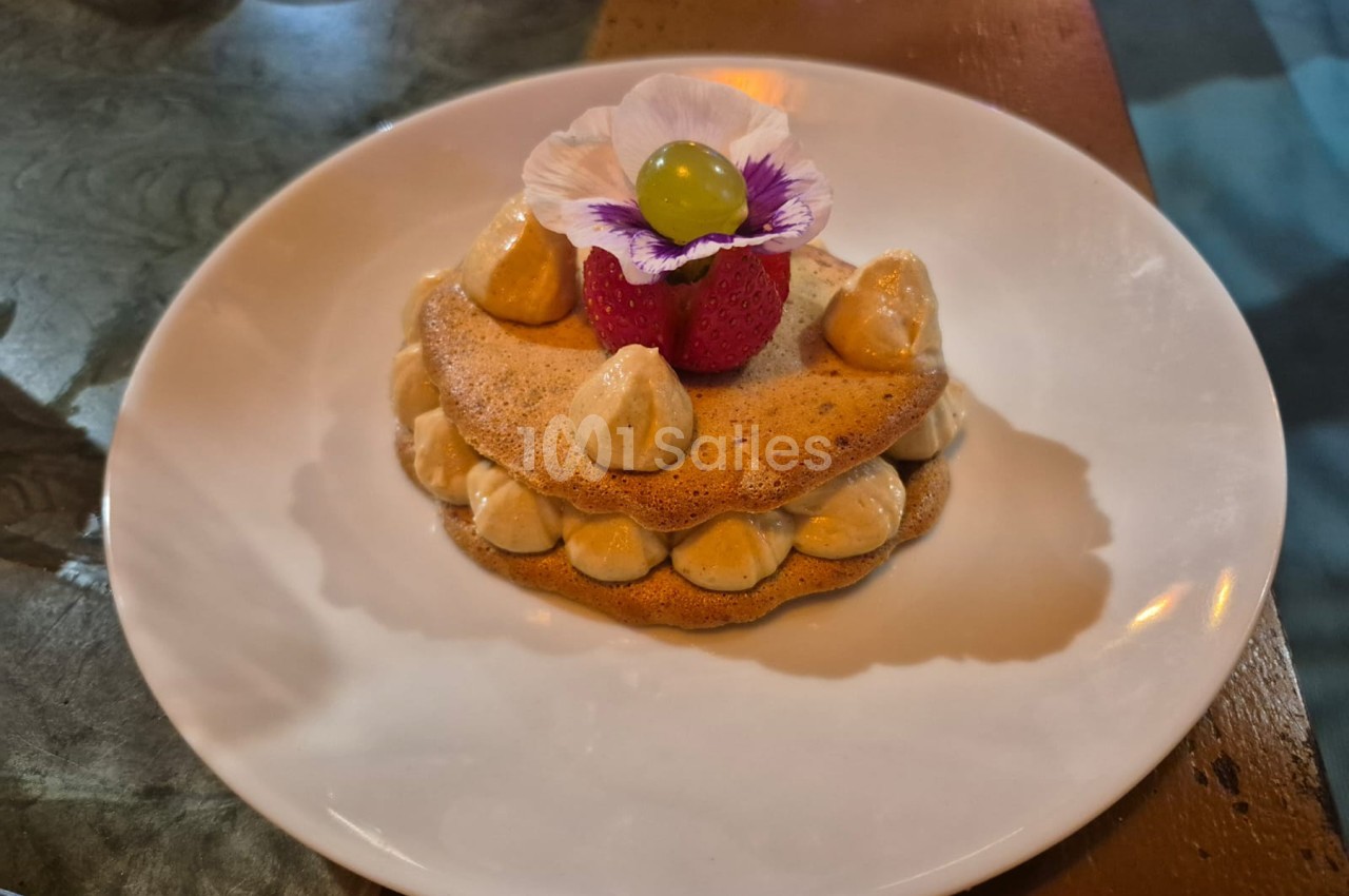 Dessert dressé sur assiette blanche - feuilletage garni de fruits, amandes grillées et fleur comestible.