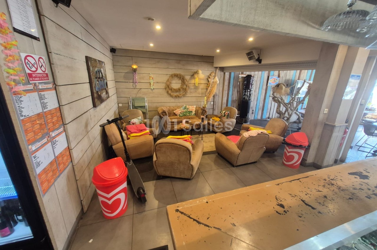 Espace intérieur avec fauteuils marron, décoration florale dorée, sièges rouges et pouf, éclairage chaud encastré.