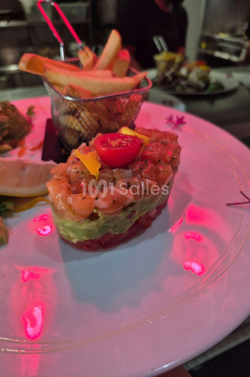 Assiette rose avec mise en place gastronomique - tartine garnie de saumon, légumes et fleurs comestibles, panier de frites.