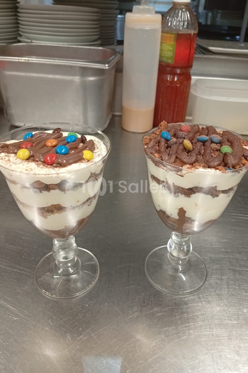 Deux coupes en verre de dessert en verrine chocolat et crème avec bonbons colorés, sur plan de travail inox en cuisine.