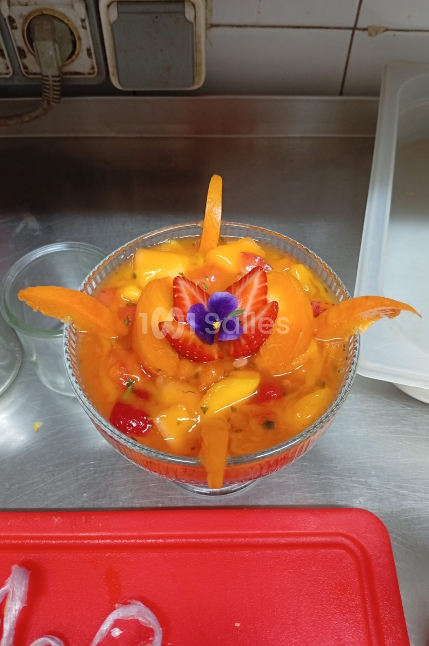 Salade de fruits tropicaux en coupe avec fraises, mangue et fleur comestible violette, en cuisine professionnelle.