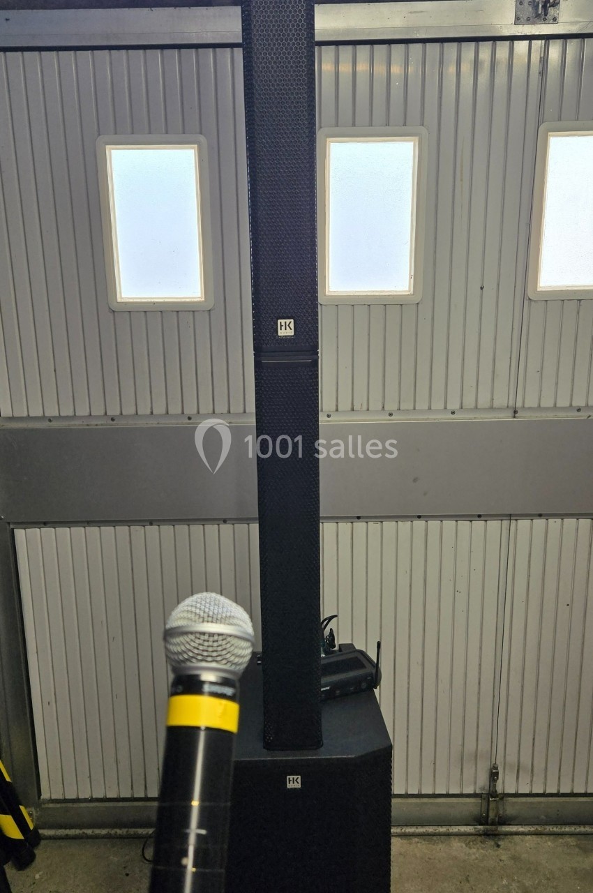 Système de sonorisation avec une colonne d'enceintes et un microphone tenu devant, installé dans un garage.