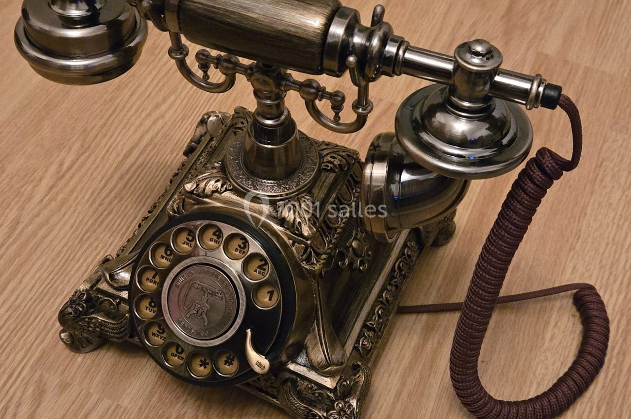Téléphone vintage en métal avec cadran rotatif et combiné, posé sur un sol en bois clair.