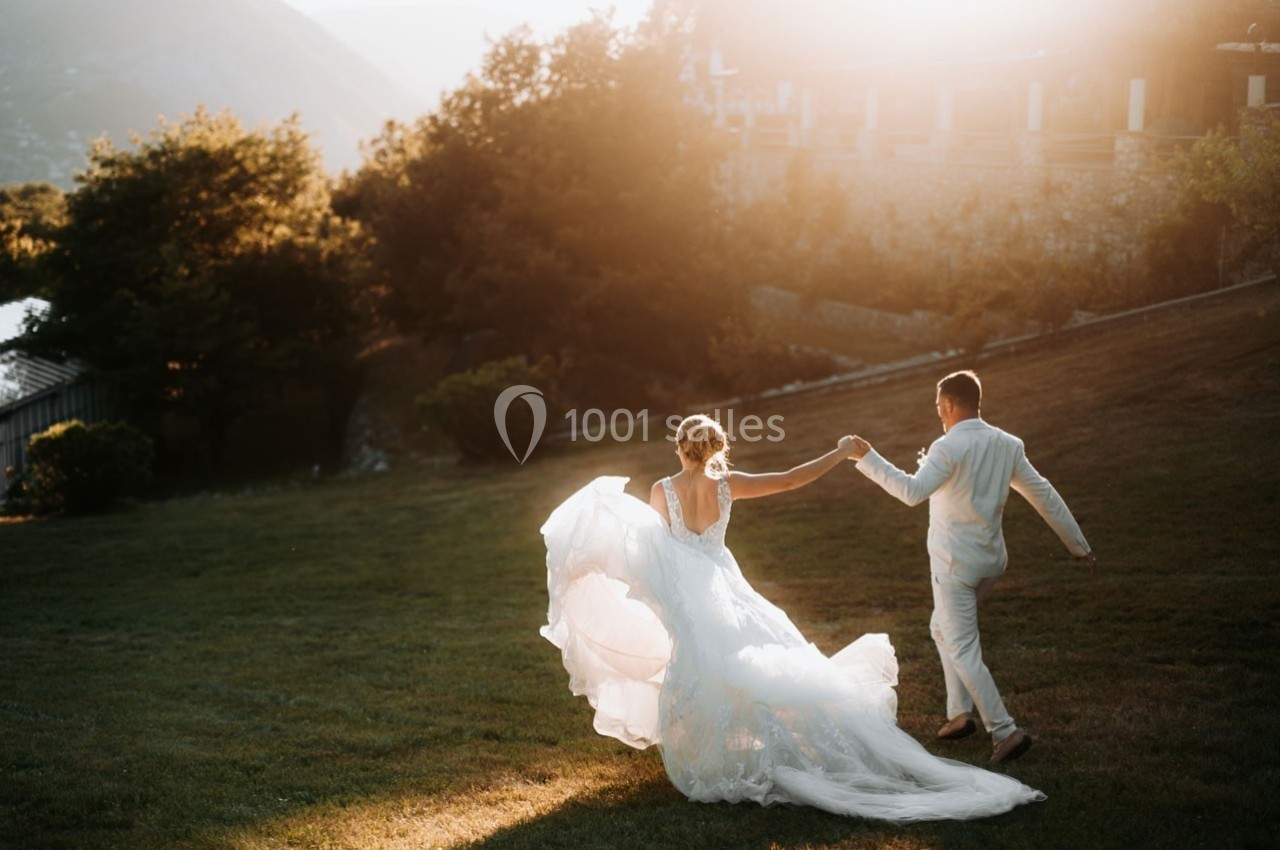 Un couple en tenue de mariage danse sur une pelouse au coucher du soleil, entouré de verdure et de lumière douce.