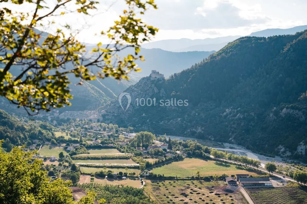 Vue d'une vallée verdoyante avec des champs, un village, une rivière et des montagnes en arrière-plan.