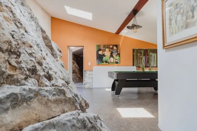 Couloir intérieur avec murs en pierre, tapis coloré au sol et vue sur une mezzanine lumineuse avec poutres rouges.
