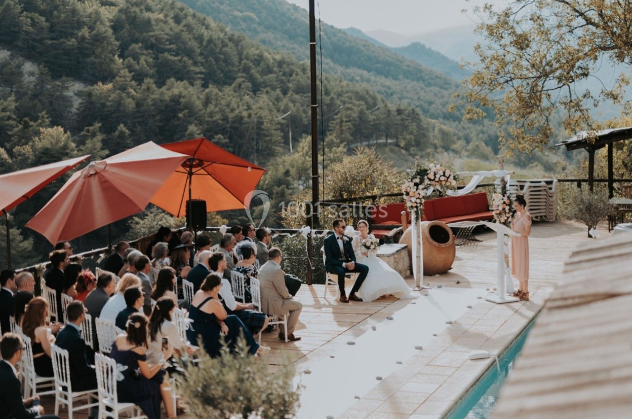 Cérémonie de mariage en plein air près d'une piscine, entourée d'invités et de montagnes en arrière-plan.