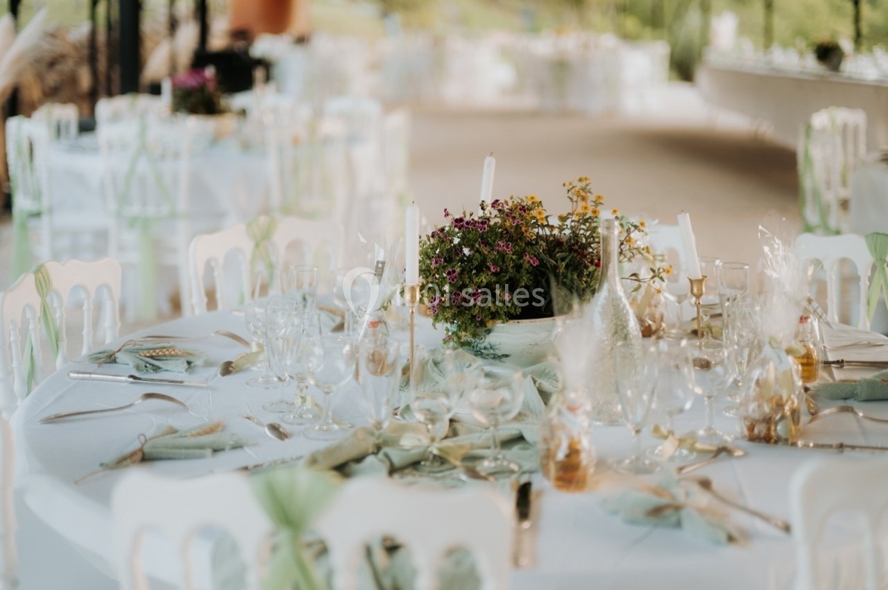 Tables décorées pour un événement avec nappes blanches, fleurs colorées et couverts élégamment disposés.