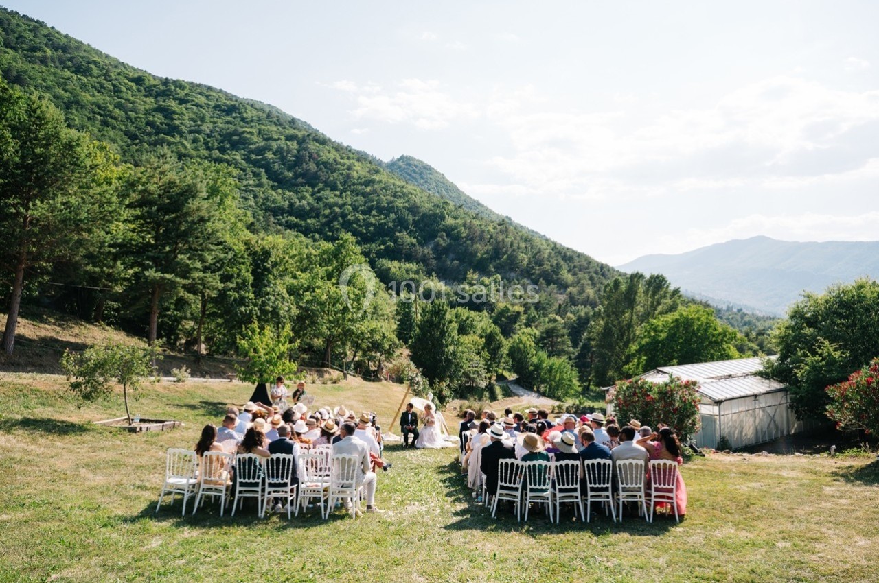 Cérémonie de mariage en plein air avec des invités assis, entourée de montagnes et de verdure.