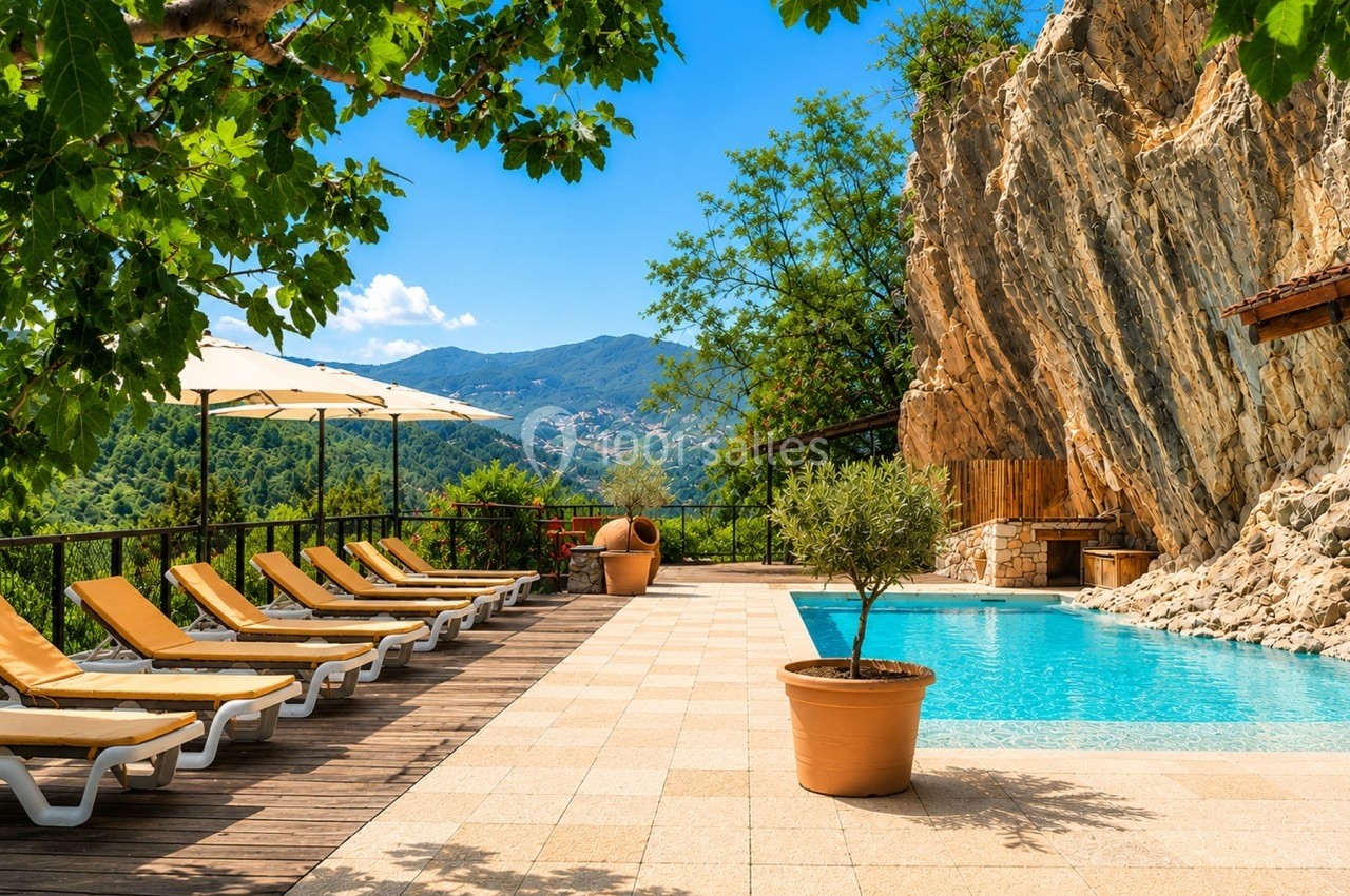 Piscine extérieure bordée de transats, entourée de rochers, végétation et vue sur des collines verdoyantes.