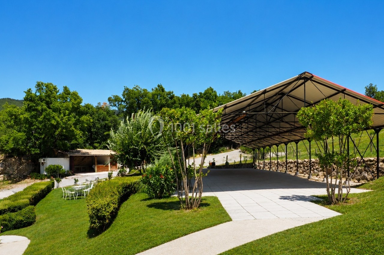 Espace extérieur avec une grande structure couverte, entouré de verdure et d'arbustes sous un ciel dégagé.