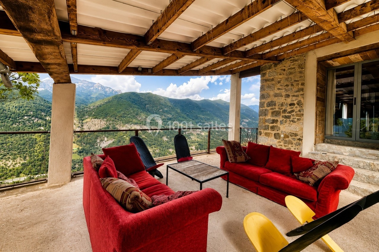 Terrasse couverte avec canapés rouges, table basse et vue panoramique sur des montagnes verdoyantes.