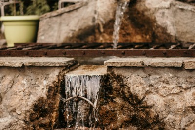 Miniature La Fontaine, crédit : livelystories Vue aérienne d'un bâtiment en pierre entouré de verdure, avec des montagnes en arrière-plan au coucher du soleil.