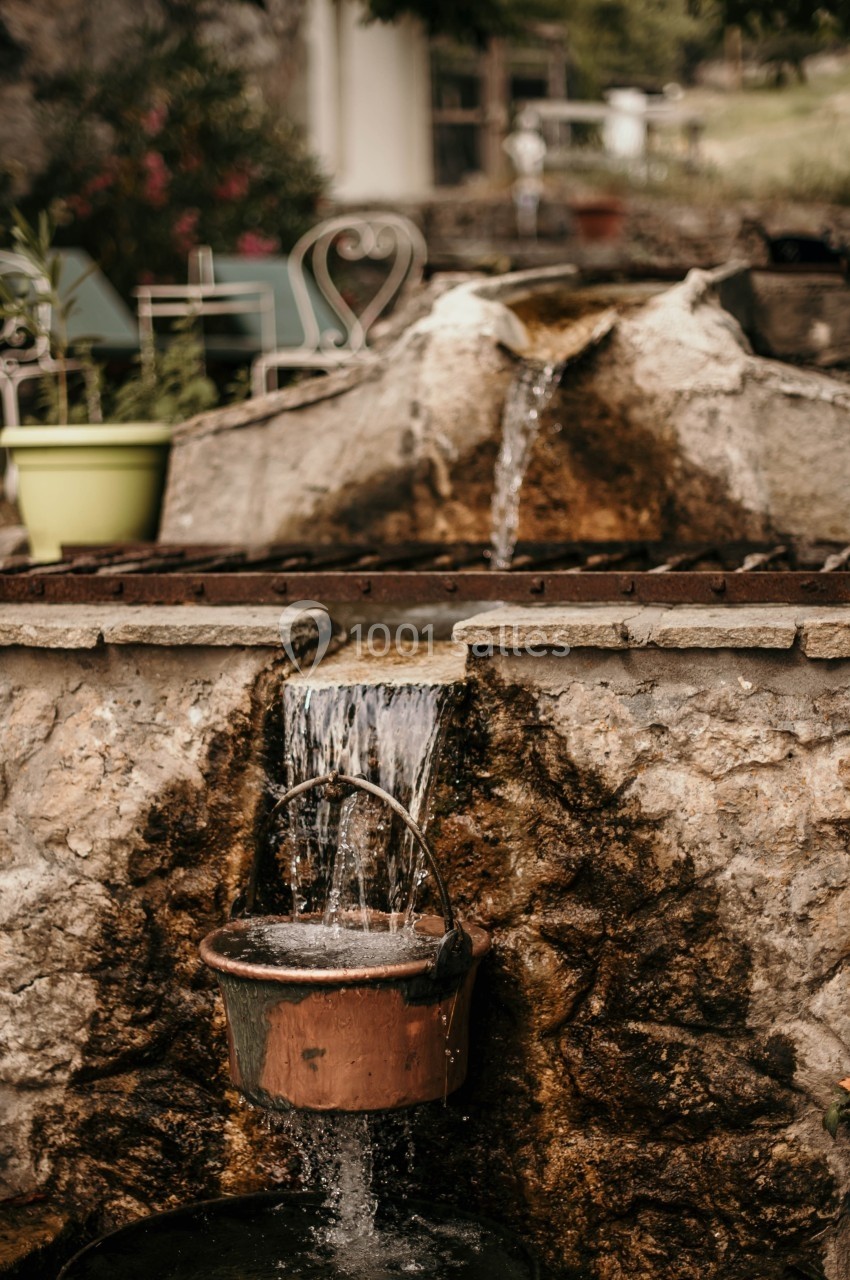 Fontaine rustique en pierre avec un seau en métal recueillant l'eau qui s'écoule en cascade.