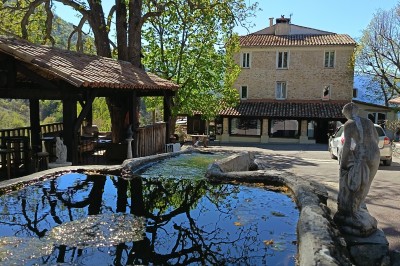Miniature La Place, vue de La Fontaine Vue aérienne d'un bâtiment en pierre entouré de verdure, avec des montagnes en arrière-plan au coucher du soleil.