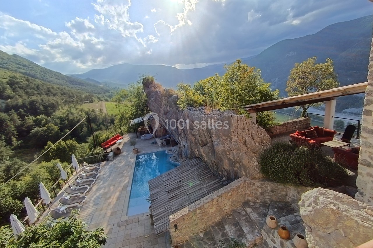 Vue d'une piscine extérieure entourée de chaises longues, d'une terrasse en pierre et de montagnes verdoyantes en arrière…