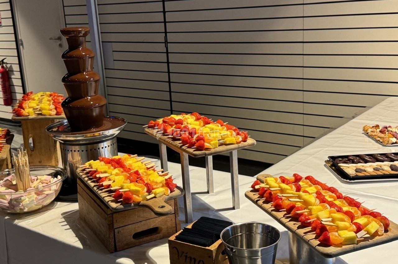 Fontaine de chocolat entourée de brochettes de fruits frais et de guimauves sur une table de buffet.