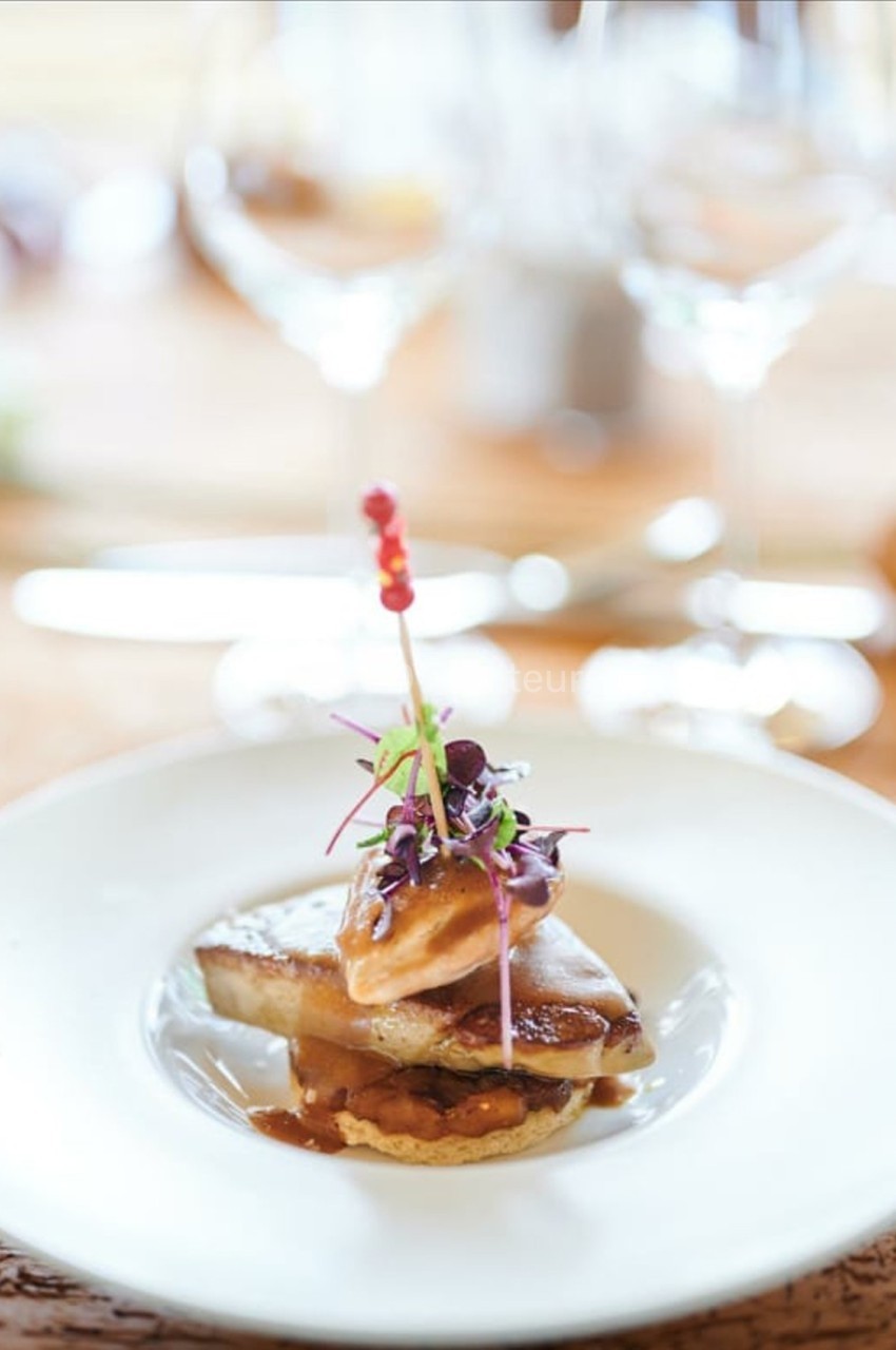 Plat gastronomique avec foie gras, micro-pousses et sauce, présenté sur une assiette blanche dans un cadre raffiné.