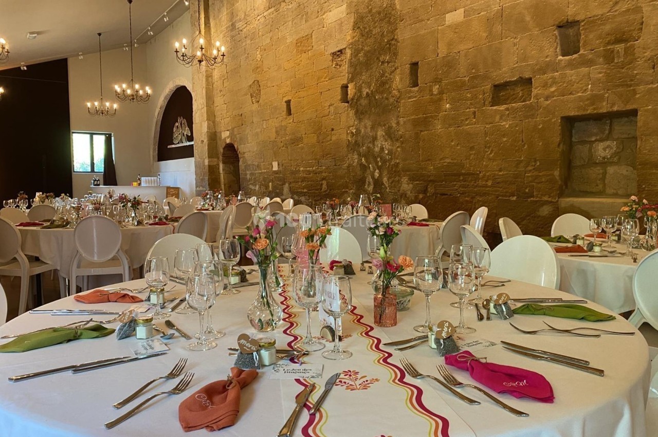 Salle de réception décorée pour un événement, avec tables rondes dressées, nappes blanches et décorations florales.