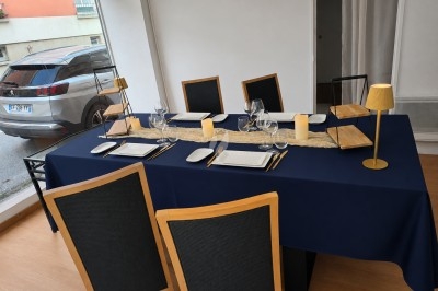 Table dressée avec une nappe bleue, vaisselle élégante, bougies et lampes dorées, dans une pièce lumineuse.