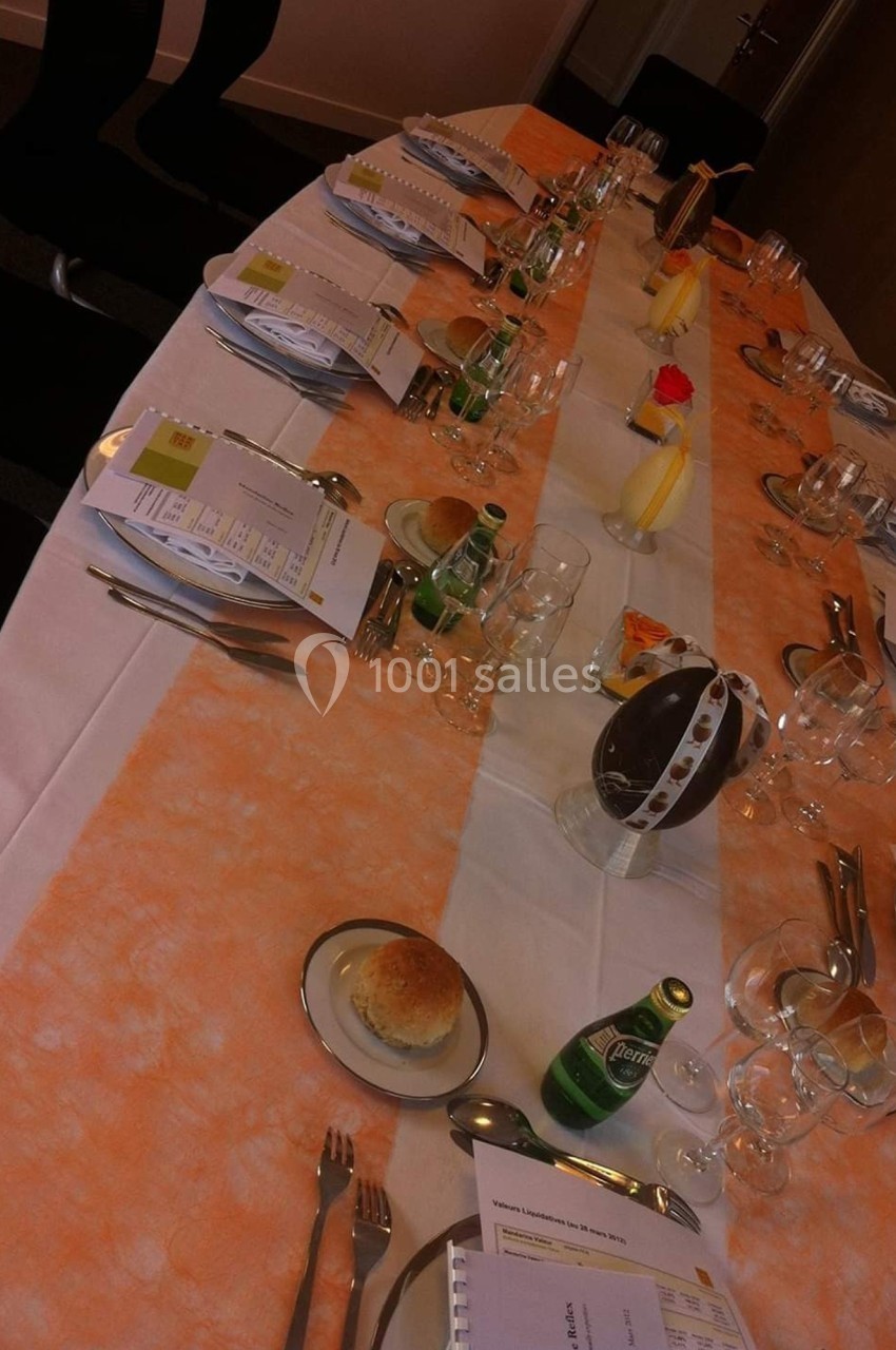 Table dressée pour une réunion ou un repas, avec documents, verres, couverts, bouteilles d'eau et décorations.