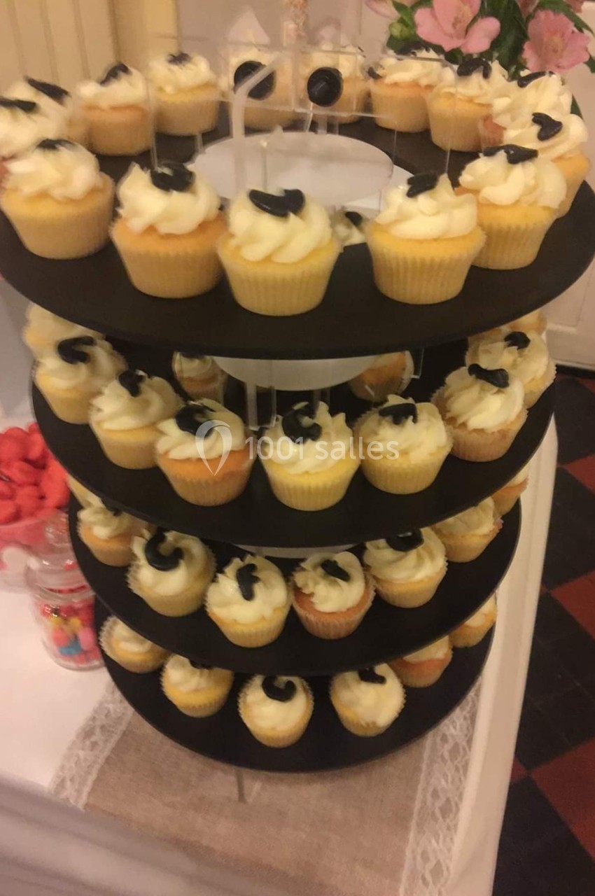 Présentoir à plusieurs étages garni de cupcakes décorés de glaçage blanc et de petites décorations noires.
