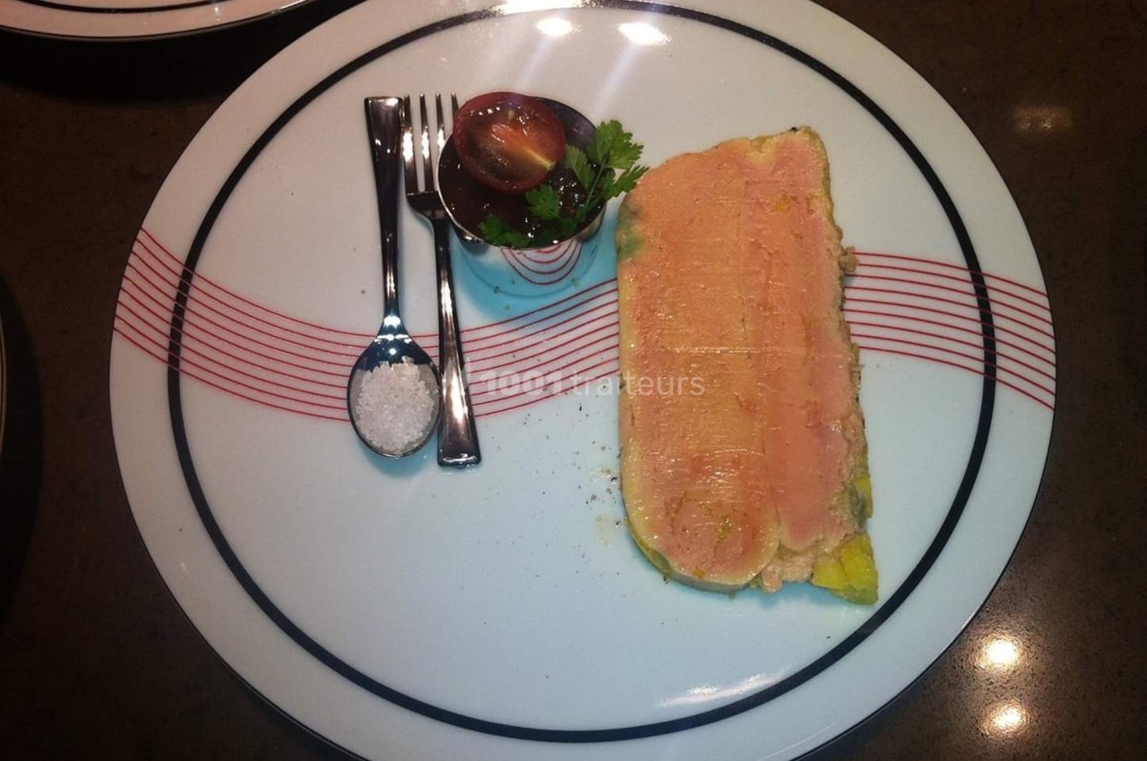 Tranche de terrine servie avec une tomate cerise, du persil, une cuillère de sel et des couverts sur une assiette décorée.