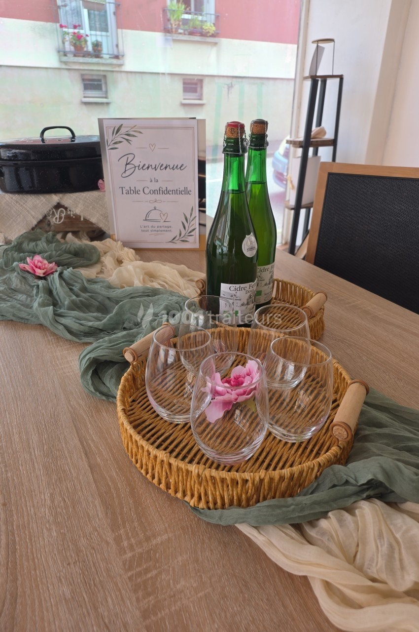 Table décorée avec des verres, bouteilles d'eau, fleurs et tissu, avec un panneau ’Bienvenue à la Table Confidentielle’.