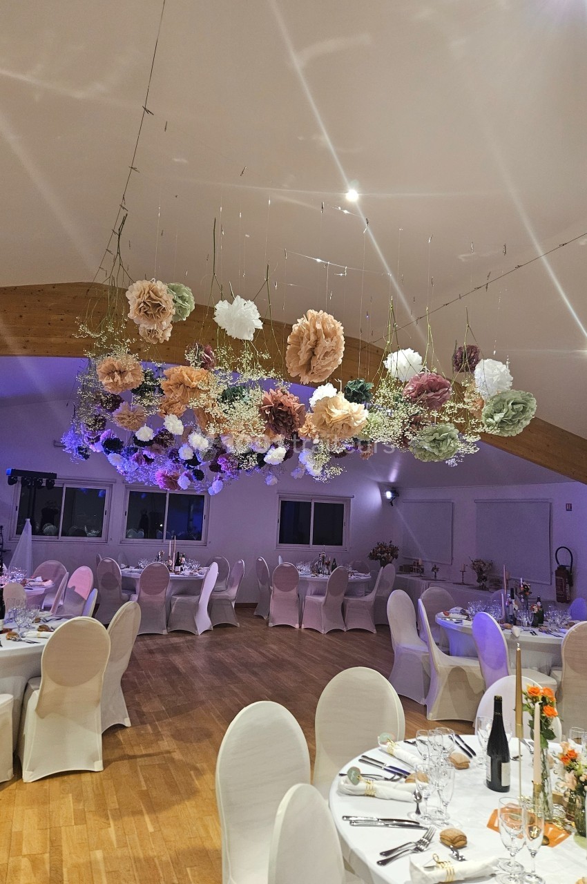 Salle de réception décorée avec des tables dressées et des fleurs suspendues au plafond.