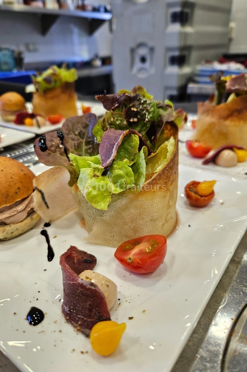 Assiette gastronomique avec salade, tomates cerises, viande séchée et sauce balsamique, servie en présentation soignée.