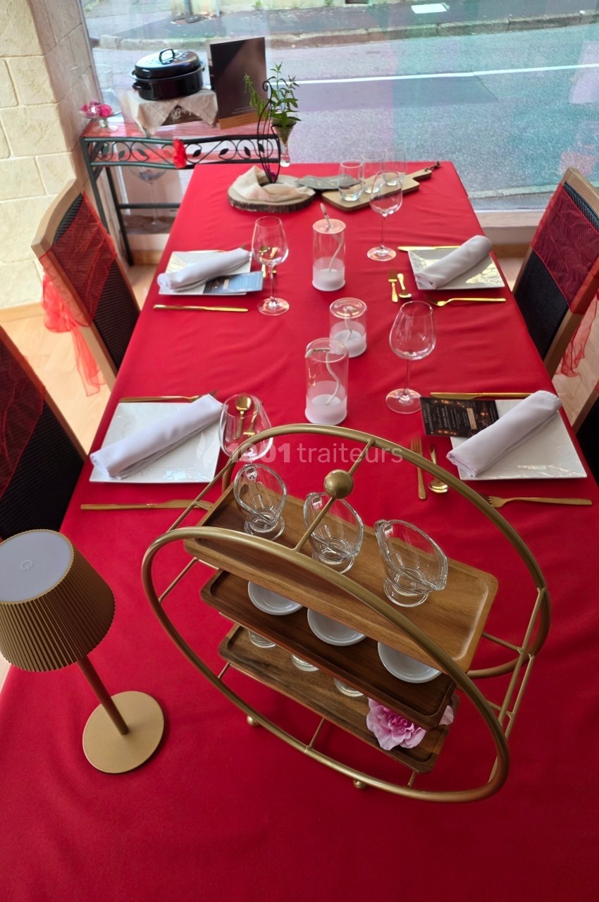 Table dressée avec une nappe rouge, vaisselle élégante, verres, serviettes pliées et un présentoir en bois au centre.