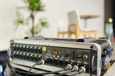 Table de mixage audio avec plusieurs câbles connectés, posée sur un rack dans un espace intérieur lumineux.