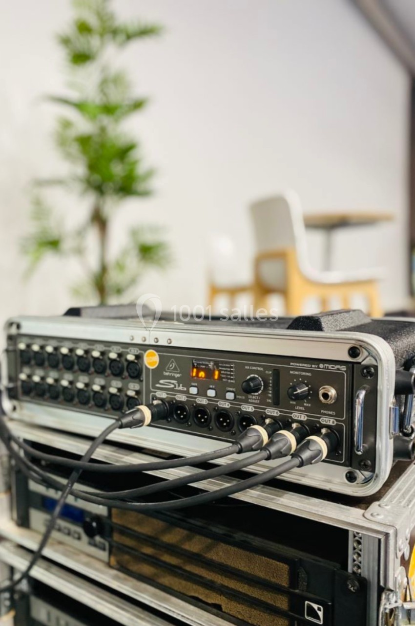 Table de mixage audio avec plusieurs câbles connectés, posée sur un rack dans un espace intérieur lumineux.