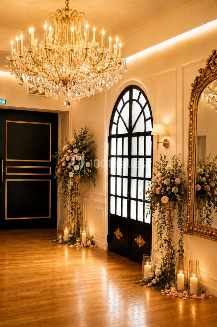 Salle élégante avec parquet, lustre en cristal, grand miroir doré, portes noires et décor floral avec bougies.