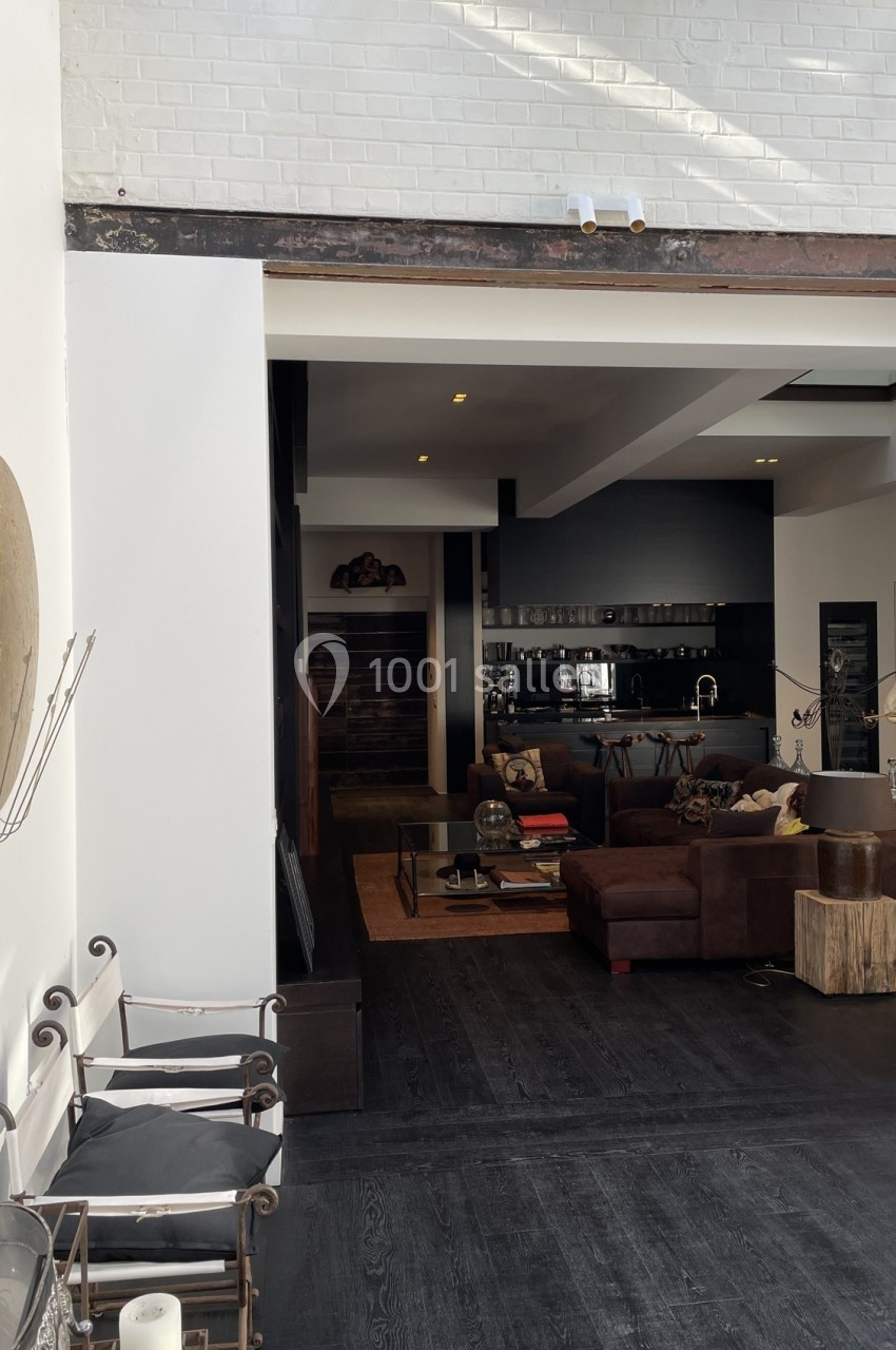 Intérieur moderne avec salon sombre, canapé en L, cuisine ouverte et murs blancs contrastants.