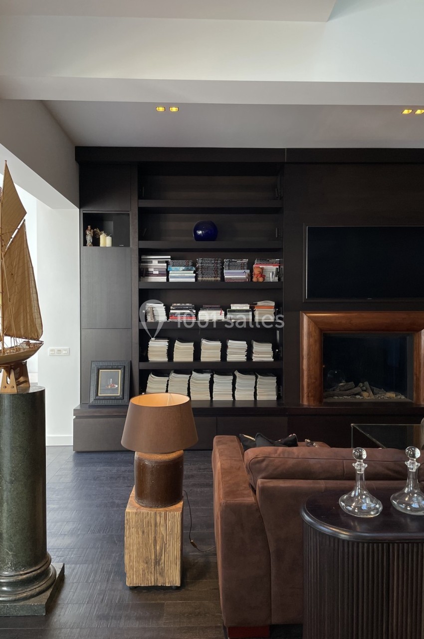 Salon moderne avec bibliothèque remplie de livres, canapé marron, lampe sur table et maquette de bateau sur un socle.