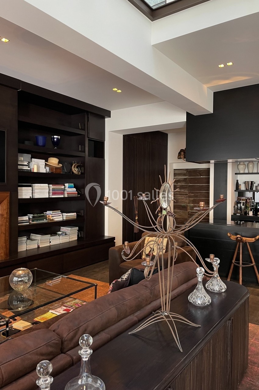 Salon moderne avec canapé en cuir, étagères remplies de livres, objets décoratifs et lumière naturelle.