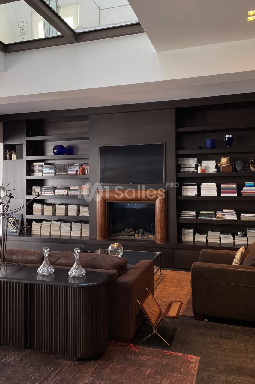Salon moderne avec cheminée encadrée de bois, étagères remplies de livres et objets décoratifs, mobilier sombre et élégant.