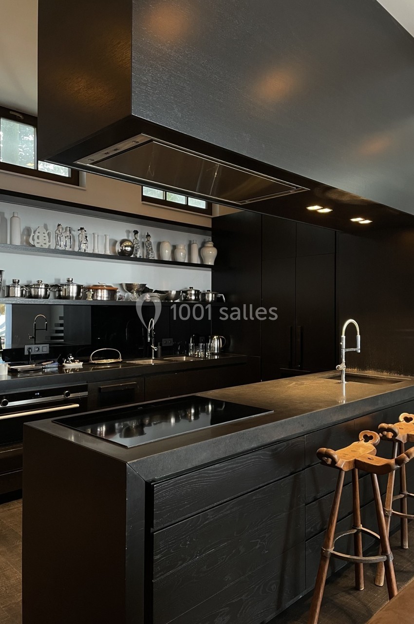 Cuisine moderne avec mobilier noir, plan de travail en bois sombre, étagères ouvertes et tabourets en bois sculpté.