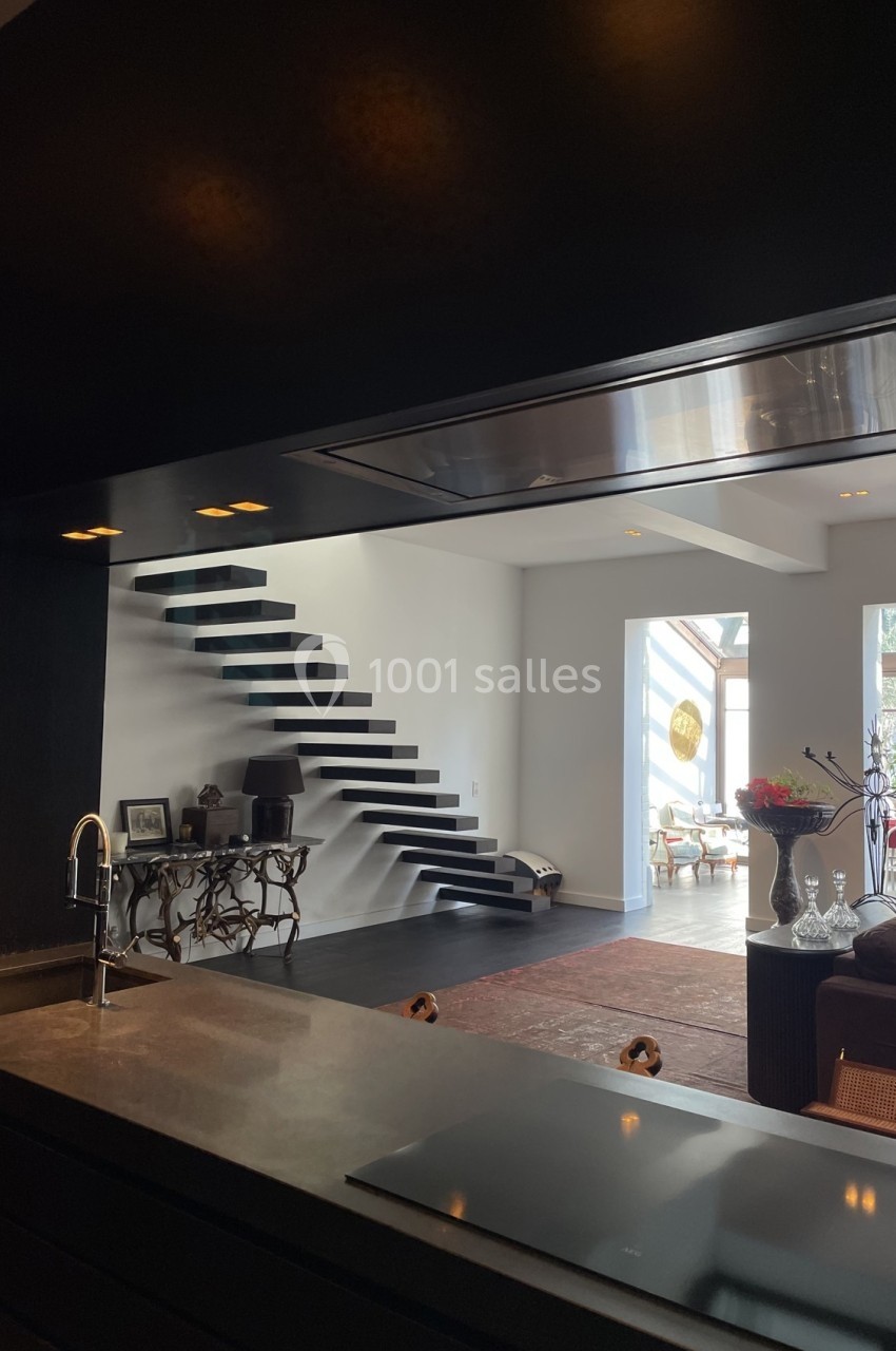 Vue d'une cuisine ouverte sur un salon moderne avec escalier flottant et grande luminosité naturelle.