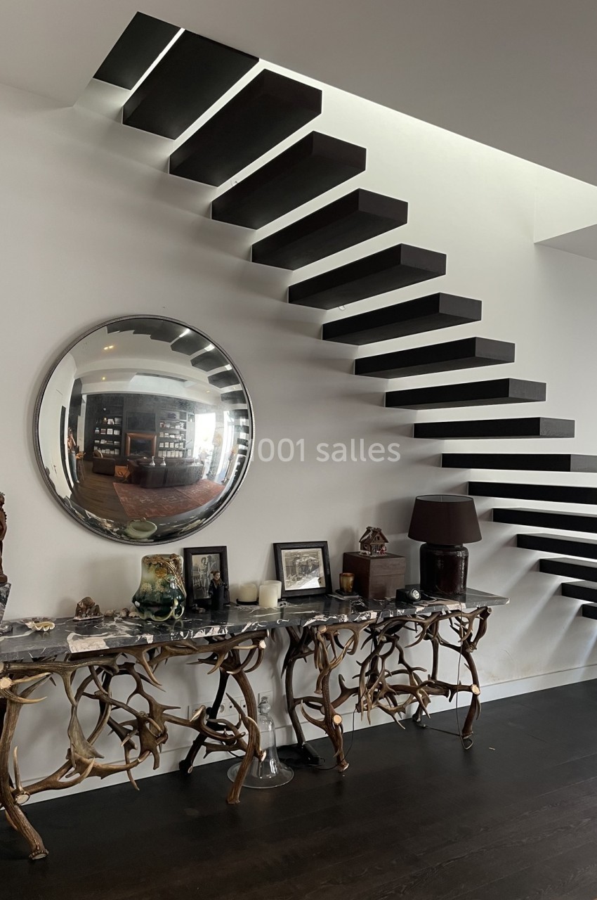 Escalier flottant noir au design moderne, avec une console ornée de sculptures et un miroir rond au mur.