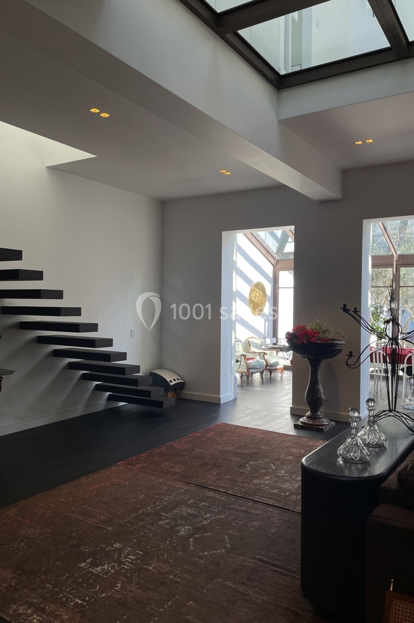 Intérieur moderne avec escalier flottant noir, grande baie vitrée et mobilier élégant dans un espace lumineux.